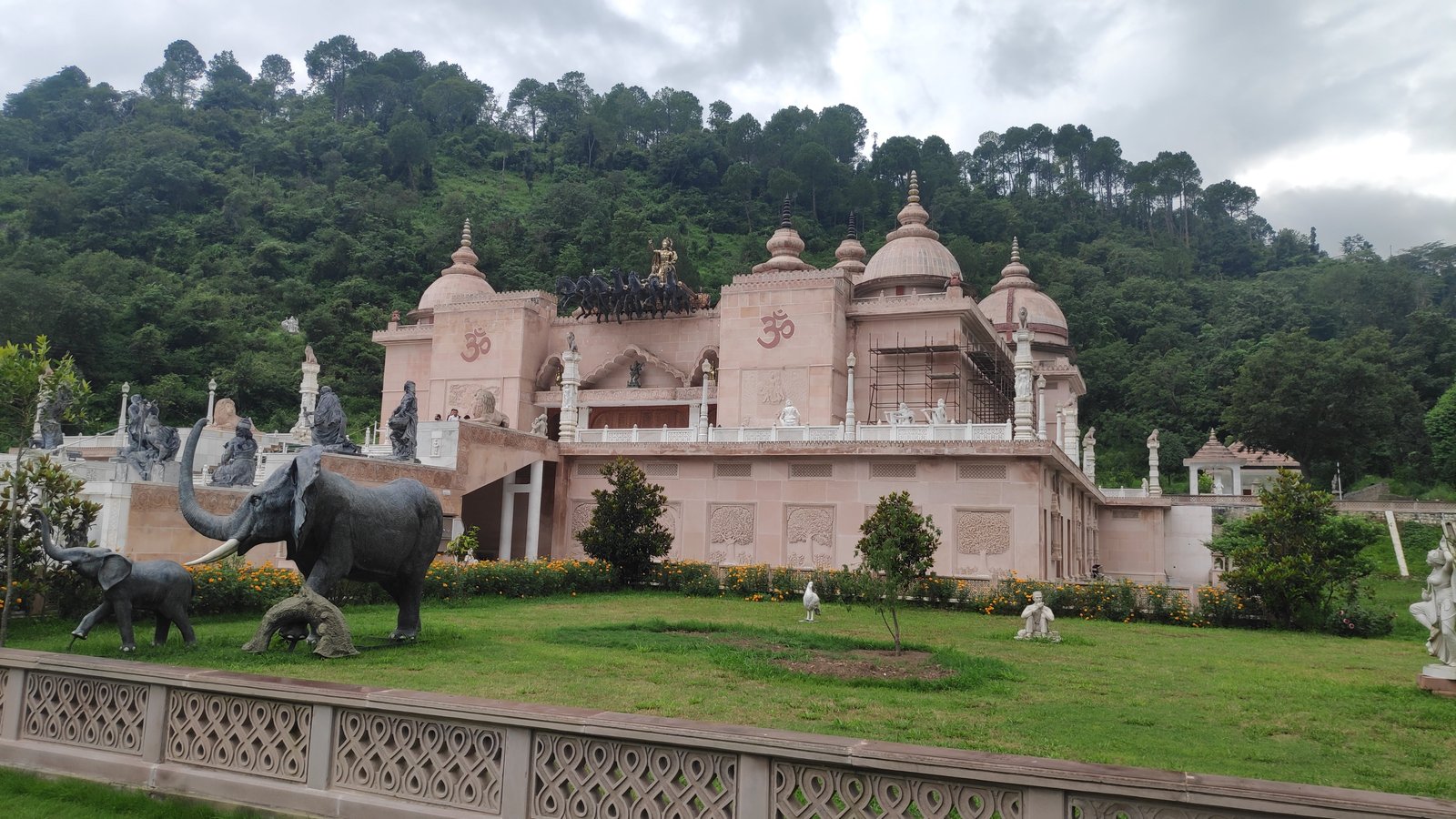 Pink sandstone temple at Mohan Shakti Heritage Park near Solan, with elephant sculptures and a wooded hillside behind it