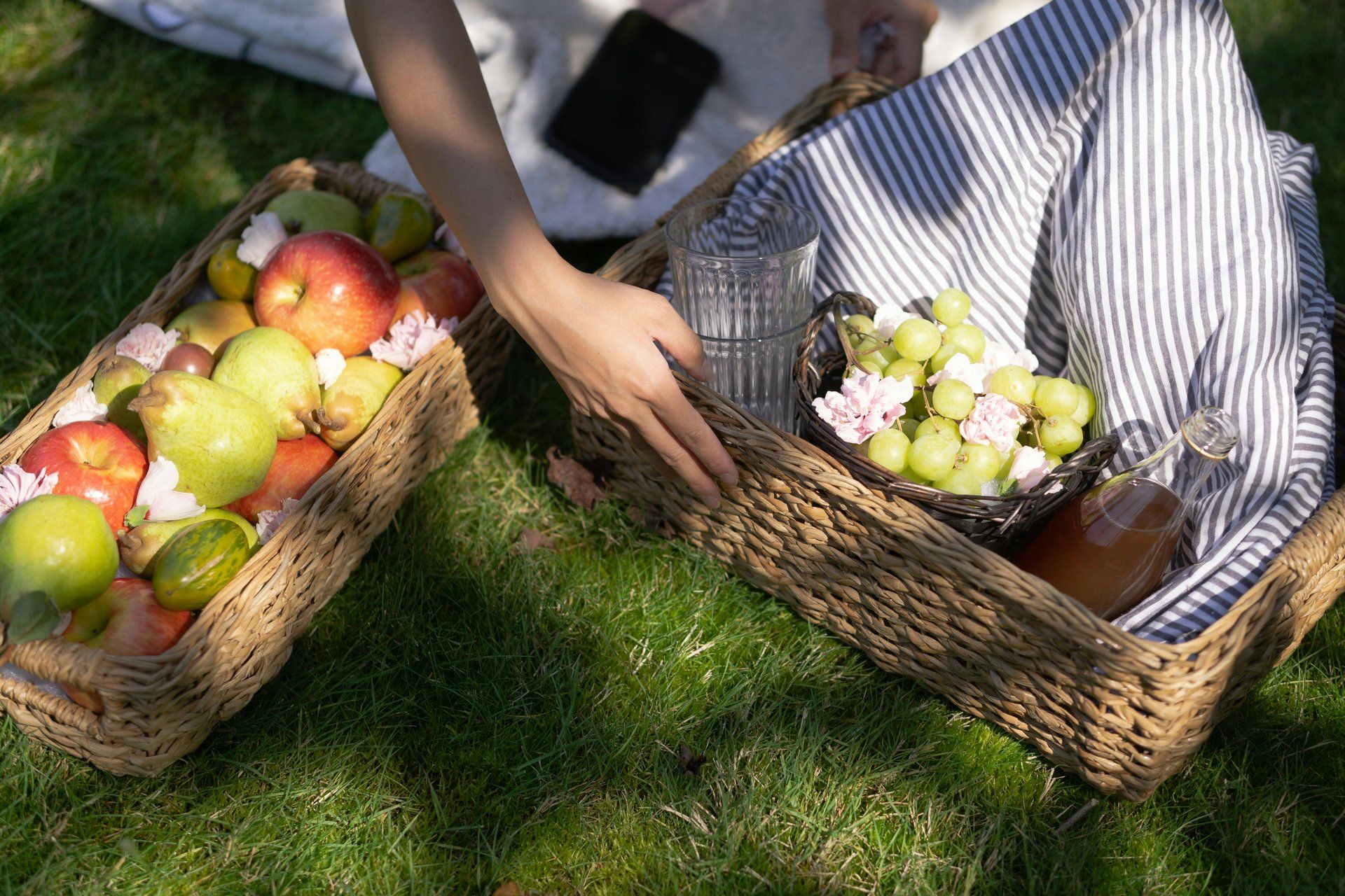 Picnic baskets of fresh fruit and drinks set out on sunlit grass