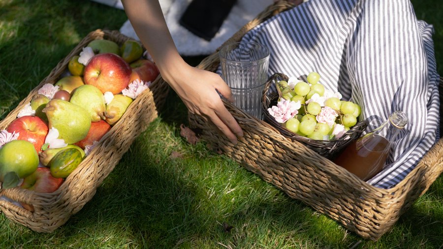 Baskets of apples, pears, and grapes on the grass for a picnic setup