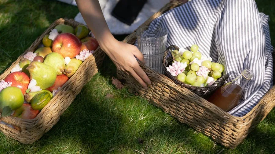 Baskets of apples, pears, and grapes on the grass for a picnic setup