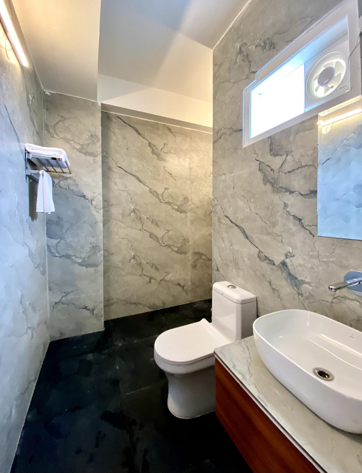 En-suite bathroom with grey marble walls, black floor, vessel basin and exhaust window