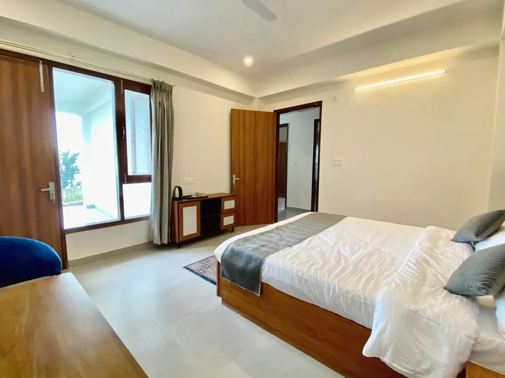 Room in natural daylight with a king bed, balcony access and a wooden side chest