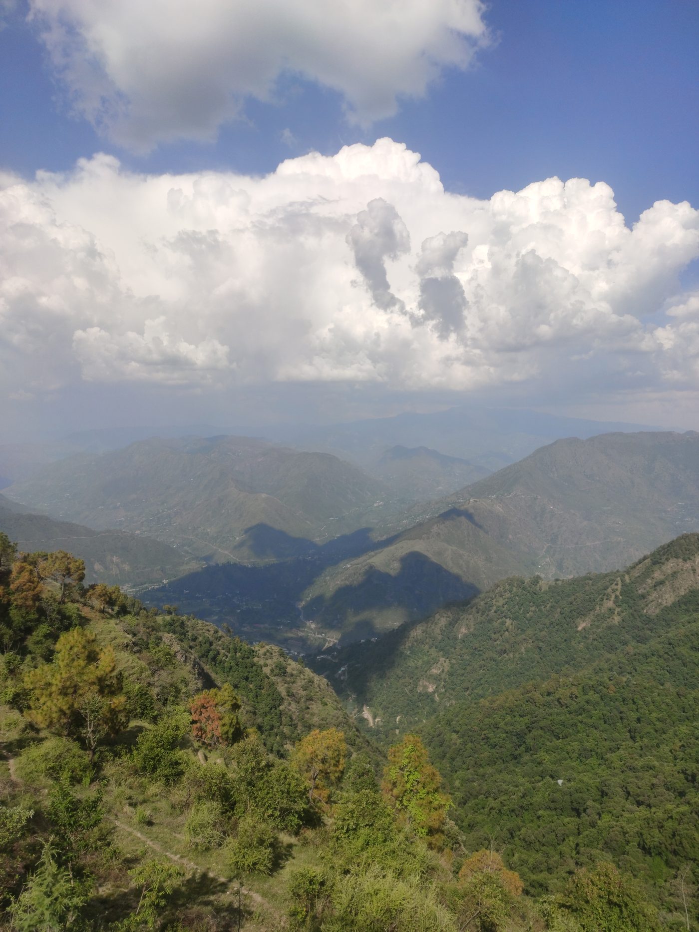 Summer cloudscape over the Himachal foothills — cumulus clouds piled over layered green ridges seen from Windmill Inn