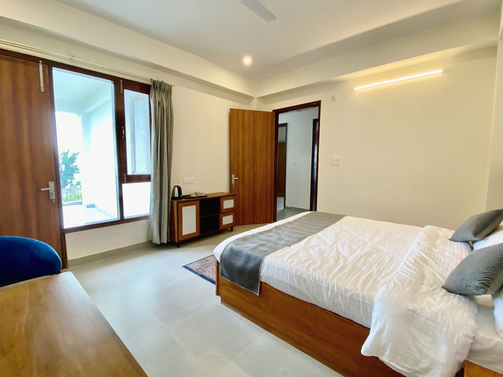Standard room interior — king bed, balcony doors letting in afternoon light, console with kettle and complimentary tea