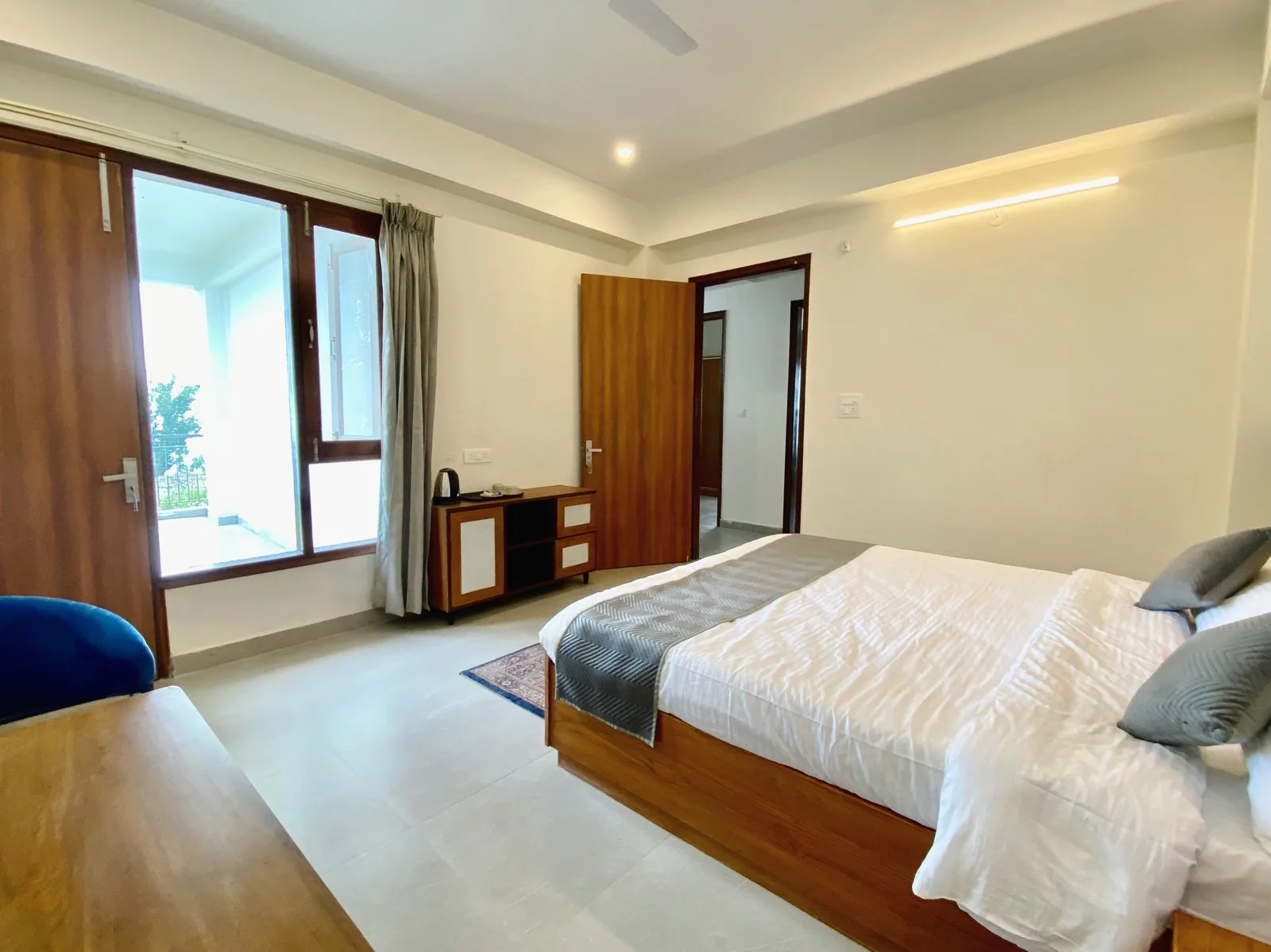 Standard room interior — king bed, balcony doors letting in afternoon light, console with kettle and complimentary tea